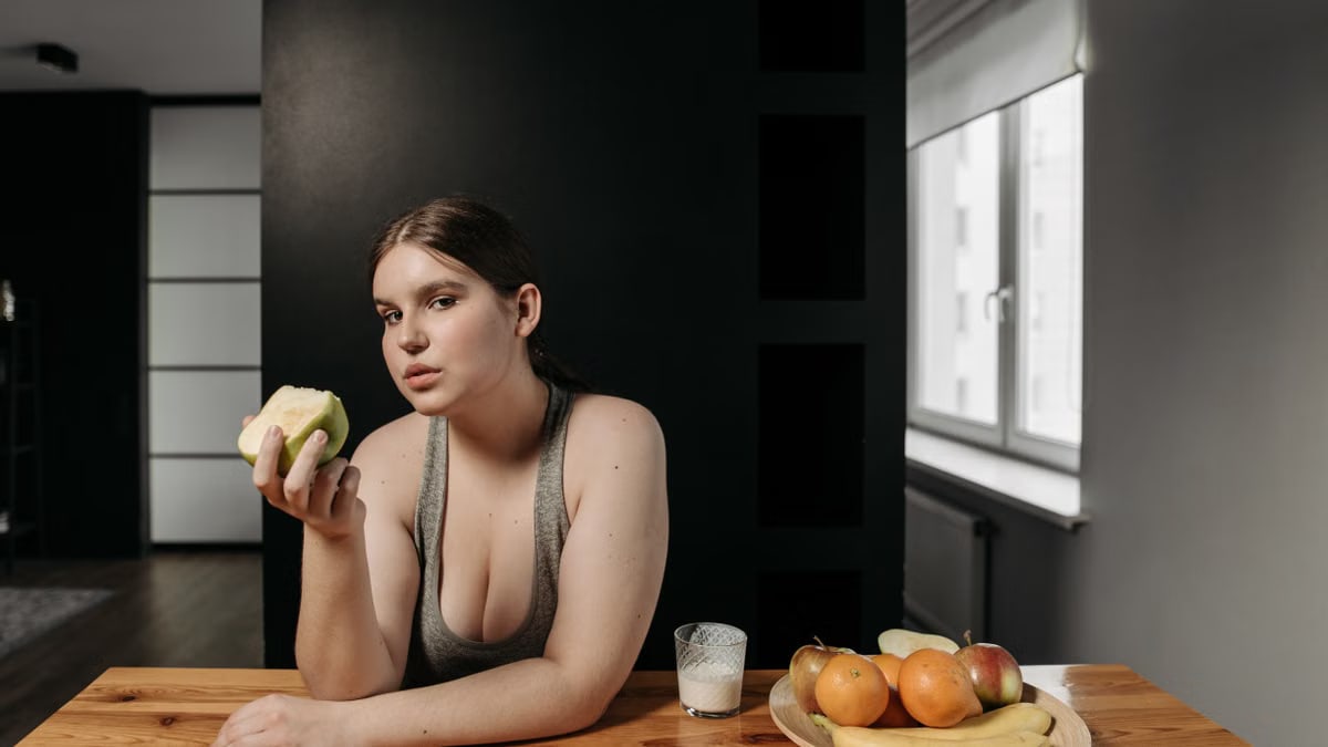 Woman enjoying an apple and glass of milk, promoting a healthy lifestyle indoors.